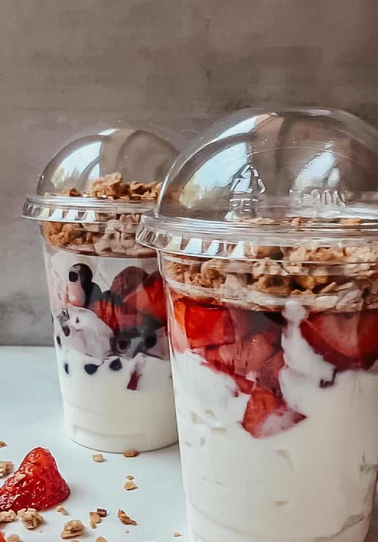 Two parfait cups with strawberries, yogurt and granola under domed lids