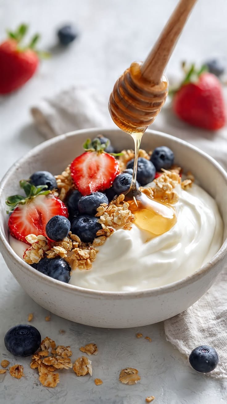 A bowl of yogurt with strawberries, blueberries, granola and honey